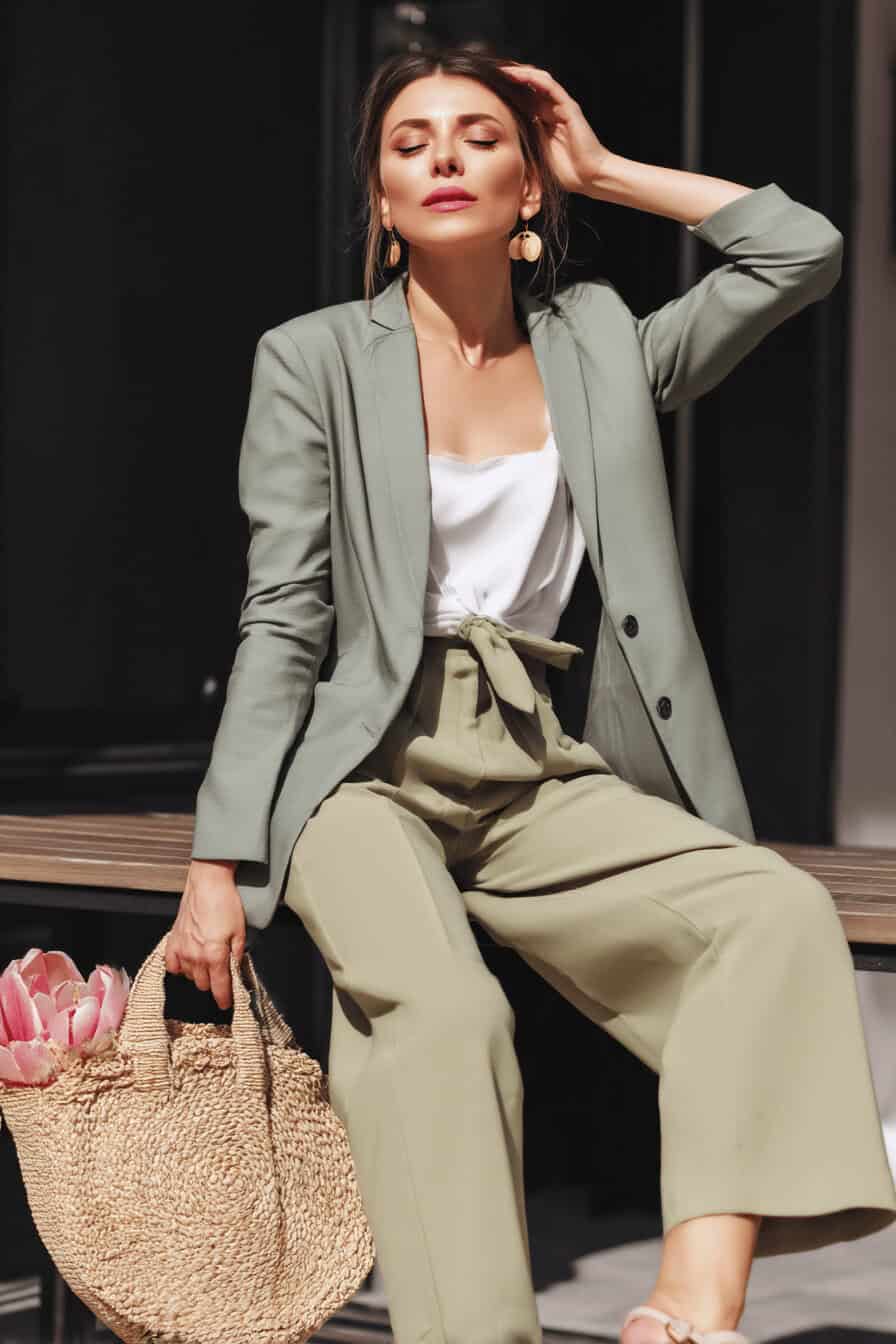 Frau in weitem Hosenanzug mit Blazer und Strohtasche.