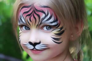 Kind mit Tigergesichtsbemalung vor Grün