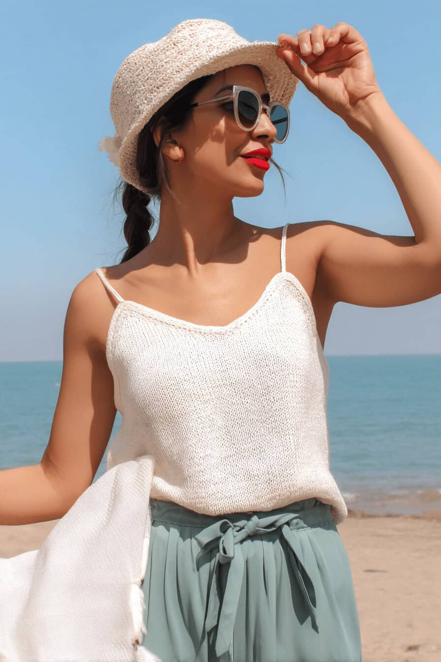 Frau am Strand mit weißem Strick-Top und Hut.