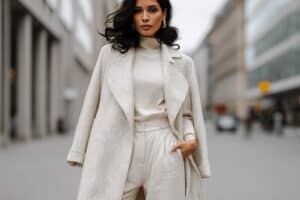 Frau in cremeweißem Winteroutfit mit Mantel und Rollkragenpullover auf einer Stadtstraße