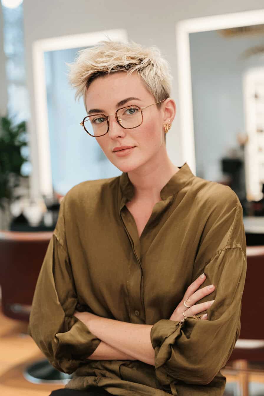Frau mit kurzen blonden Haaren und Brille in einem Salon.