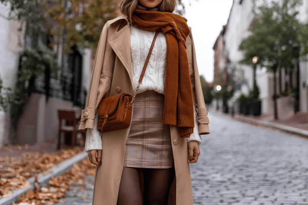 Frau trägt herbstliches Date Outfit mit Trenchcoat, Karo-Rock und Strickschal