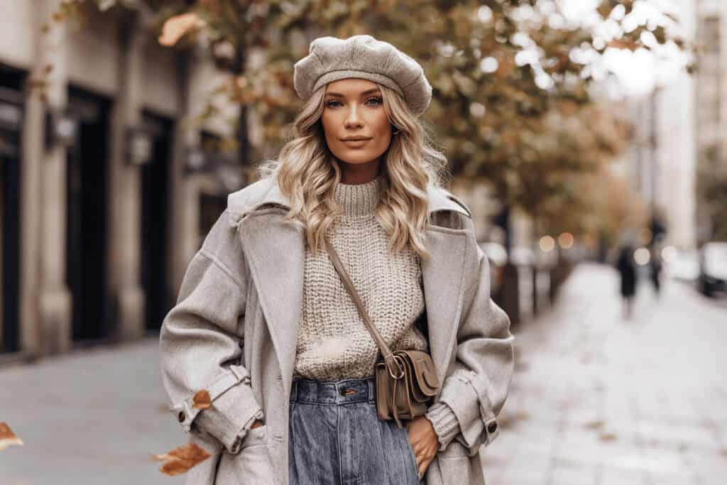 Frau mit beigem Mantel, Strickpullover und Jeansrock im herbstlichen Straßenbild