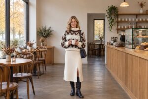 Frau in cremefarbenem Strick-Midirock und Norwegerpullover mit Kaffeetasse in einem Café